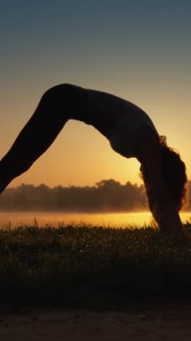 Doğa 'nın gücünü her yoga hareketinde açık havada idman yaparak hisset. Gün batımında bir kadının silueti ve dikey bir videoda doğanın güzelliği. Hayatta başarı ve kendini kontrol ve disiplin.