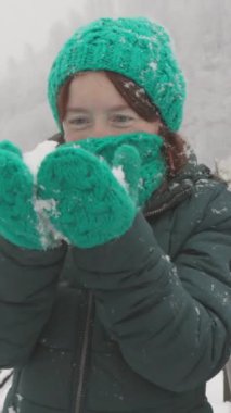 Dağların karlı arka planıyla köprüde yapılan kış yürüyüşünün büyüleyici güzelliği gerçek bir tatil ve kış masalı hissi veriyor. Eldiven takmış, karla oynayan bir kadın.