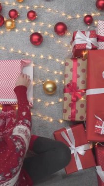 Noel atmosferinde, bir kadın her kutuyu sarıyormuş gibi yapar, sevgi ve şefkat dolu hediyeler yaratır. Noel ağacı ağzının altında, bir kadın hediyeleri özenle sarar.