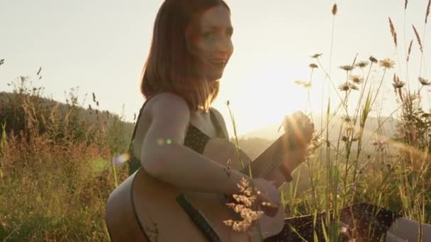 在大自然中 在露天 一个年轻的女人在弹吉他中找到了休息和快乐 当吉他手喜欢在高山草坪上弹奏吉他时 浪漫的气氛充满了整个空间 — 图库视频影像