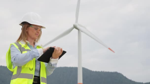 風力エネルギーの影響 女性デザイナーはタブレットを使用して風力発電所を建設する予定です エネルギーへのグリーン代替 タブレットを有する女性は 風力タービンの環境影響を研究します 高品質で — ストック動画