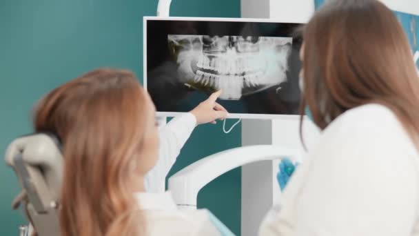 歯科医は診断のために患者のX線を示しています 歯科医は 歯と歯茎のトモグラフィーの結果を患者に説明する 患者はXを分析するときに歯医者を信頼します — ストック動画