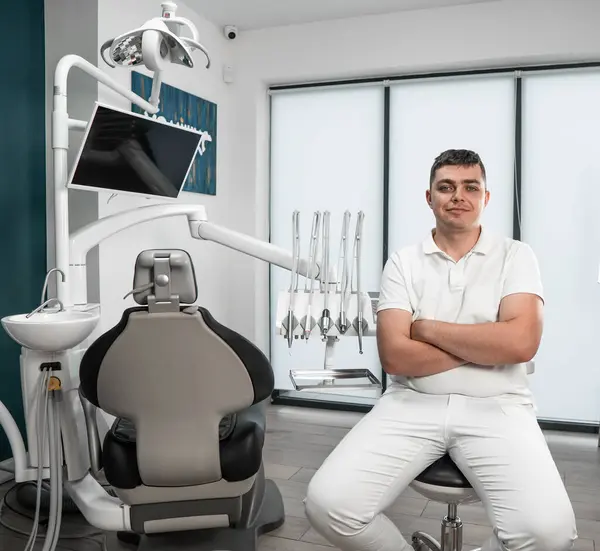 The dentist sits with his hands closed. A dentist in a modern clinic is ready for treatment and consultations. Installation of dental implants is a modern method of restoring teeth in a dental center