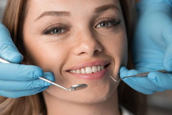 Beautiful and beautiful woman at the dentists appointment. Close-up face looking and smiling at the camera. Dentists hands with instruments near patients smile and teeth. Dental Clinic Treatment