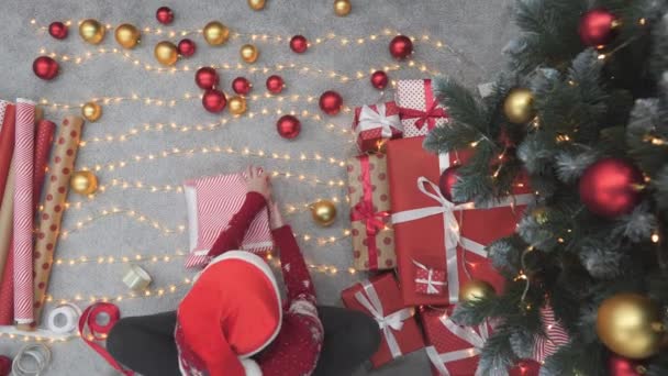 在温暖舒适的房子里 一个年轻的女人在准备圣诞礼物 她穿着一件舒适的毛衣 小心翼翼地把礼物包装在五彩缤纷的盒子里 每件礼物都是 — 图库视频影像