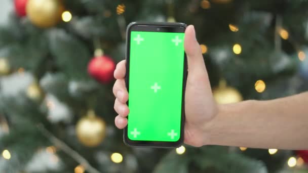 照らされたクリスマスツリーとスマートフォンは ホリデーシーズン中にオンラインショッピングや予約のガイドです グリーンスクリーンとクロメイク効果 高品質の4K映像 — ストック動画