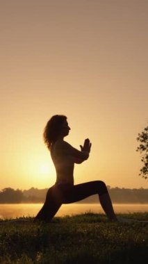Yoga, fiziksel ve ruhsal uyumu sağlamak için bir araçtır. Bir kadın, yoganın büyüsünü doğal ortamında keşfeder. Gün doğumunda kişisel gelişim ve psikofiziksel gelişimin dikey videosu