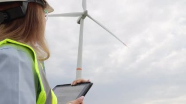 Tabletle donatılmış bir kadın mühendis yeşil enerjiye doğru önemli bir adım olan yel değirmeninin gücünü inceler ve analiz eder. Türbindeki bilimadamı dijital tabletle etkin gelişiyor
