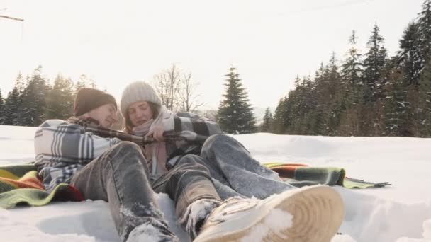 ブランケットでのエンターテイメントと軽い会話の陽気な瞬間は 冬の森でカップルの深い感情を強化します 雪の中の毛布の上に 夫婦は温かい飲み物を共有しています — ストック動画