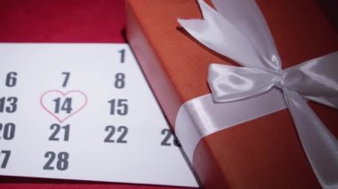 Romantik Sevgililer Günü Hediyesi kırmızı bir kumaşta dekoratif bir hediye paketi yatıyor. 14 Şubat tarihli bir takvim. Aşkın şenlikli atmosferi. Yüksek kalite 4k görüntü