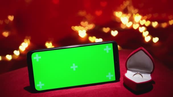 赤い背景に金のダイヤモンド リングが付いている宝石箱の近くのスマートフォンのクロマのキー効果 ウェブサイトと携帯電話のモバイルアプリのレイアウトとしての緑色の画面 オンラインストアとオンラインショッピング — ストック動画