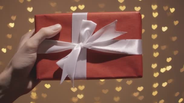 ビデオはバレンタインデーにぴったりのプレゼントです ギフトパッケージは手で保持しています 彼らは金色のLedハートで照らされ それはの祝賀に特別な魅力を与えます — ストック動画