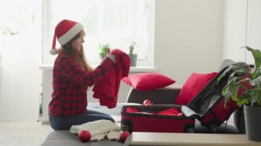 Bir kadın yeni yıl tatili için mantralar hazırlar. Kış seyahati ve tatil. Noel Arifesi Kızı 'nda Noel Baba şapkasıyla bavul katlamak. Yüksek kalite 4k görüntü