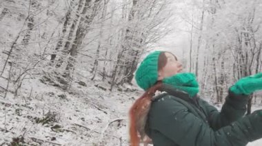 Bu kış ormanında, genç bir kadın elindeki kar tanelerine bakmak için durdu. Bu genç kadın, kış ormanının tazeliğinden ilham alıyor ve ilkini yakalamak için ellerini kaldırıyor.