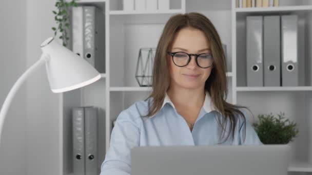 喜びに満ちた笑顔で 女性は仕事の過程で 机のラップトップで幸せと笑いを見つける 自宅で居心地の良いオフィスで働くメガネの美しいビジネスマン インターネット — ストック動画