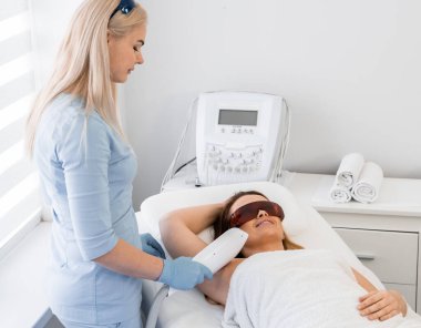 Deneyimli bir kozmetik uzmanı ve fotokopi prosedürü bir güzellik salonunda deriyi yumuşatmak ve derin bir rahatlık sağlamak için. Kadın prosedür sırasında dinlenip rahatlıyor. Hasta uzanır ve gülümser.