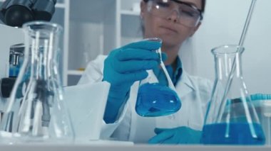 Biyoloji merkezindeki bir laboratuar asistanı örnekleri test ve moleküler analiz için dikkatlice hazırlıyor. Koruyucu eldiven giyen bir kadın elinde kimyasal matara tutuyor. Yüksek