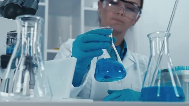 生物中心的一名实验室助理认真研究这些样品 准备进行测试和分子分析 手里拿着化学瓶 戴着防护手套的女人 — 图库视频影像