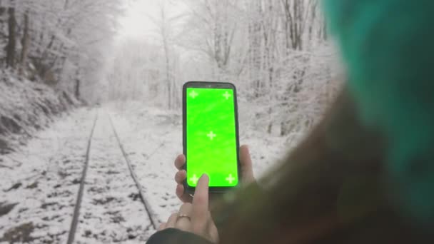 女性は冬の森を歩き クロマのキー効果で携帯電話を持って歩きます 年末年始の冬季のスマートフォンのグリーンスクリーン 冬休みについて 高品質の4K映像 — ストック動画