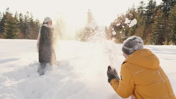 一对年轻夫妇在雪地里玩雪球 互相扔雪 在新年假期和圣诞节假期 年轻人在大自然中玩得很开心 高质量的4K镜头 — 图库视频影像