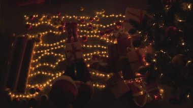 Noel ağacı ışıkları ve süslemeleriyle çevrili karanlık bir odada bir kız oturuyor. Noel süslemeleriyle çevrili olan kadın, hediye kıvırma sanatını icra ediyor.
