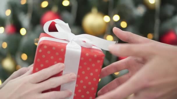 クリスマスツリーと点滅するガーランドを背景に 人々は新年とクリスマスの贈り物を交換します パッケージボックスを手で閉じる手 冬休みのお祝いについて — ストック動画