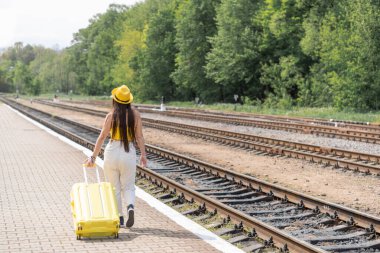Zarif sarı giysiler içinde hevesli bir turist, uzun zamandır beklenen yolculuğunu bekliyor, elinde bavuluyla. Tren istasyonunun platformunda bavulla yürüyen bir kadın. Yüksek kalite