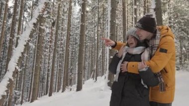 Aşık bir çift, ormanda romantik bir yürüyüş sırasında güzel kış manzarasının tadını çıkarıyor. Uzakta bir yerde elini ve parmağını ona doğrultuyor. Kış tatili Yüksek kalite 4k görüntü