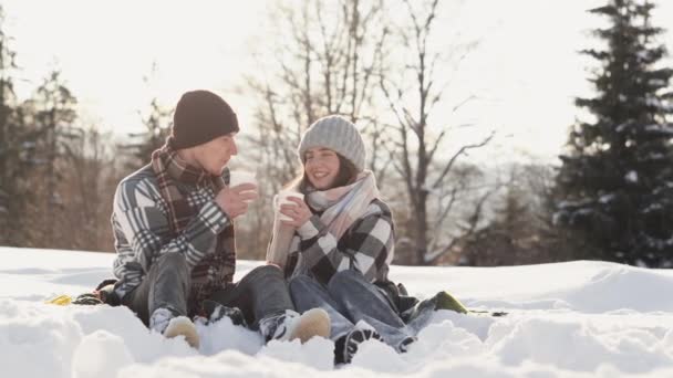 愛好家は冬のピクニックを楽しんでいます ホットドリンクや料理は 雰囲気に暖かさと優しさを追加します カップルは雪のスポットに座って計画を議論しながら冬の朝食を節約します — ストック動画