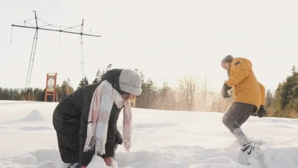 恋人は雪の中で遊び 雪玉を投げ 雪に覆われた枝の下で面白い数字を作ります 遊んで雪を投げるのも楽しい 恋するカップルは山の頂上に座り ジョイントを楽しむ — ストック動画