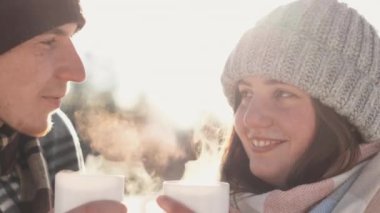 Close-up of a guy and a girl smiling.Young couple happy together on vacation in nature holding hot drink in their hands steaming in frosty winter air. Brain-to-heart conversations and heart-to-heart