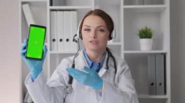 Spot ışıkları altında hasta sağlığına bakan doktor, yüksek kaliteli tıbbi hizmetler sunarak çevrimiçi video konferansları ve konsültasyonlar düzenler. Telefondaki krom anahtar ve yeşil ekran, web sitesinin tanıtımı, uygulama ve