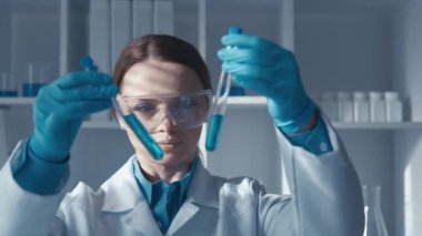 Test tüpleri ve araştırma ekipmanlarıyla gelişmiş laboratuardaki dikkatli kadın bilim adamı. Bu video, çalışma gözlüklü bir bilim adamının sağlam bir araştırma yürüttüğü tıbbi araştırmanın özünü yakalıyor.