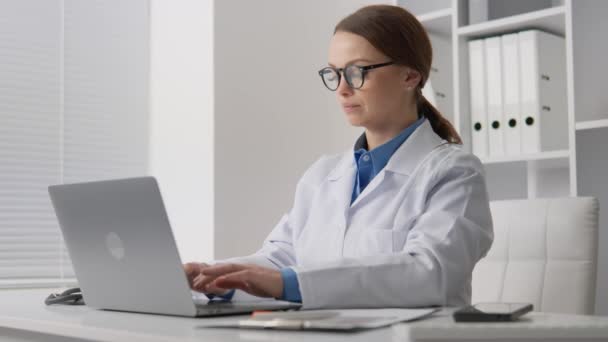 オフィスで働いていた医師は 肯定的な結論を書き 電子文書を扱いました 女性医師が医療データをノートパソコンにオンラインで入力します 高品質の4K映像 — ストック動画