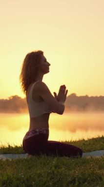 Bireysel gelişim ve yoga yoluyla doğayla uyum. Yeşil bir çimenlikte yoga yaparken odaklan ve rahatla. Kadın yoga eğitmeniyle dikey video. İç Potansiyelin Uyanışı. Yüksek