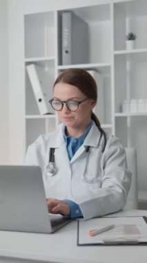 Steteskop kullanan kadın doktor laptopa odaklanmış, tıbbi verileri analiz ediyor ve klinikteki her hasta için kişiselleştirilmiş tedavi planları geliştiriyor. Beyaz önlüklü ve gözlüklü doktor. Yüksek kalite