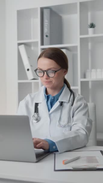 女医生与听诊器工作的重点放在笔记本电脑 分析医疗数据和制定个性化治疗计划的每一个病人诊所 身穿白衣戴眼镜的医生 高质量的 — 图库视频影像