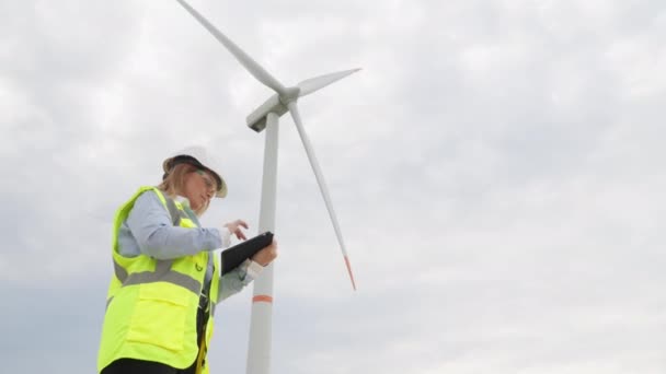 持続可能な未来のための現代のツール 女性科学者の手にタブレットと風車が緑の電力の鍵です グリーンエネルギーの源としての風力発電機 女性デザイナー — ストック動画