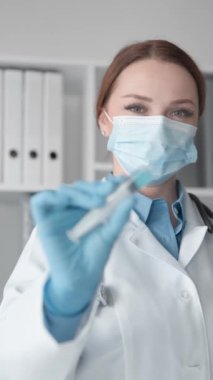 Tıbbi pratiğe dengeli bir yaklaşım gösteren ve bir ilacın kullanımına hazırlanmaya odaklanan bir tıp uzmanı. Tıbbi maskeli kadın doktorun elinde tuttuğu yakın çekim şırınga.