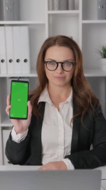 Ofiste çalışan iş kadını elinde telefonla beb web sitesi veya mobil uygulamanın yeşil akıllı telefon krom ekran reklamının yanı sıra promosyon ve ürün veya hizmetleri gösteriyor. Yüksek