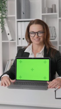 Kendine güvenen iş kadını gülümseyerek dizüstü bilgisayar ekranı gösteriyor, krom anahtar etkisiyle ev ofisindeki yeşil ekranı izliyor, işini güvenle yönetiyor. Yüksek kaliteli FullHD görüntüler