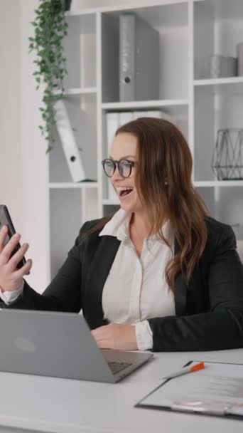 精力充沛的女商人一边看着电话一边为好消息感到高兴 一边在办公室的电脑前工作 为公司的财务目标规划战略行动 优质Fullhd — 图库视频影像