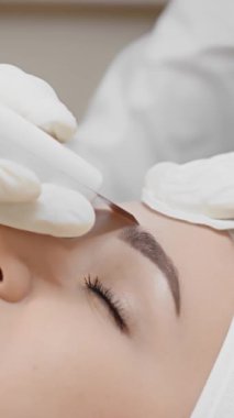 Müşteri, ultrasonik yüz temizleme sırasında hoş duygular hisseder. Dikey videoda yakından çekilir. Güzellik kliniğinde nemlendirilmiş ve tazelenmiş hisseder. Yüksek kaliteli FullHD görüntüler