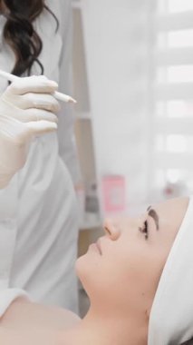 Genç bir kadın, gözlerindeki ve yüzündeki kırışıklıkları azaltmak için botulinyum enjeksiyonu yapan bir güzellik uzmanının ofisinde kanepede yatıyor. Güzellik uzmanı işaretler yapıyor.