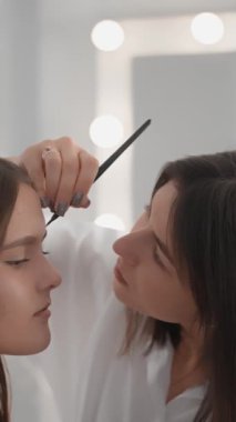 Modern bir kozmetoloji atölyesinde kadın bir kozmetikçinin ışık ve gölgelerle nasıl oynadığına bakın. Dikey video. Bu seçici güzelliği vurgulayan gerçek sanat. Yüksek kaliteli FullHD görüntüler