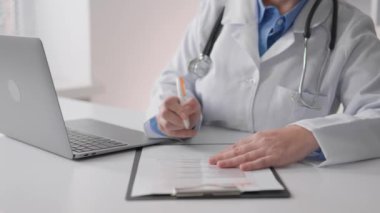 Klinikteki bir masada çalışan kadın doktor kâğıt tablete bilgi yazıyor. Doktor, bu bilgiyi hastaları etkin bir şekilde tedavi etmek ve desteklemek için kullanarak optimal çözümler buluyor. Yüksek