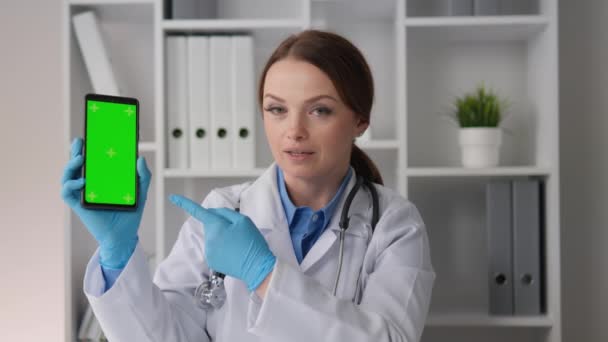 クロマキーテンプレートグリーンスクリーンスマートフォンは ウェブカムを介してオンライン相談を行う医師女性が保有し 高品質で手頃な価格の医療を提供します 彼の手で画面にポイント — ストック動画