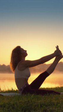 Göl kenarında, bir kadın yoga yapıyor, bu da doğal ortama daldığında rahatlamasına ve rahatlamasına yardımcı oluyor ve sakin ve iç huzurunu hissediyor. Yüksek kalite 4k görüntü