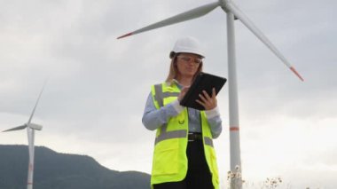 Dijital tabletli bir mühendis rüzgar türbinlerinin çalışmasını izleyerek rüzgar enerjisi merkezli santrallerin verimli ve kesintisiz çalışmasını sağlıyor. Yüksek kalite 4k görüntü