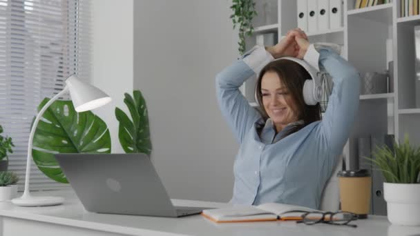 女性が働いているデスクで居心地の良い快適な職場で ノートパソコンとノートブックで勉強しています 明るいオフィスにいる女性は 仕事をうまく終えたので笑っている — ストック動画